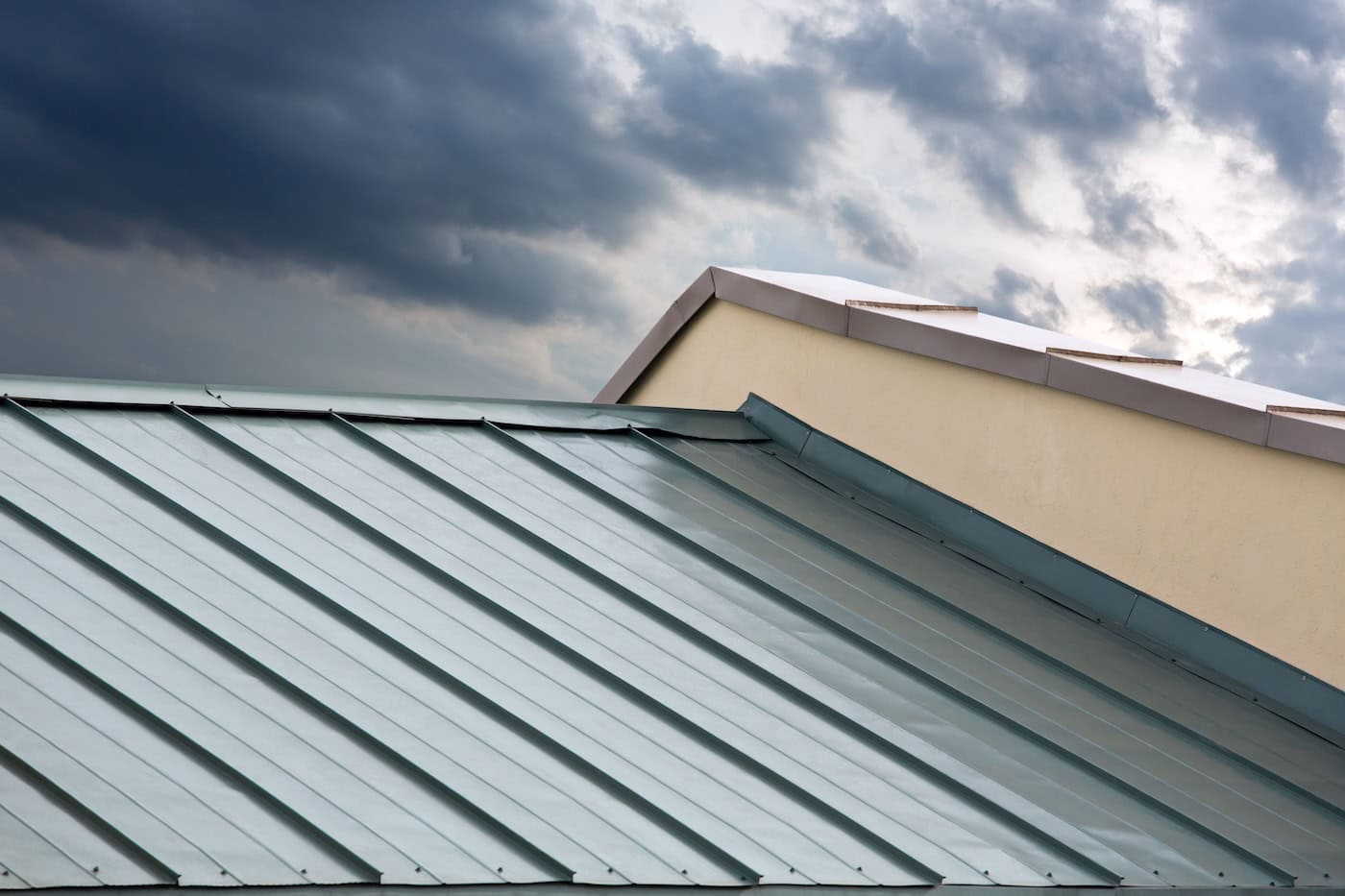 Light blue metal roof panels meet a gable end under dark storm clouds